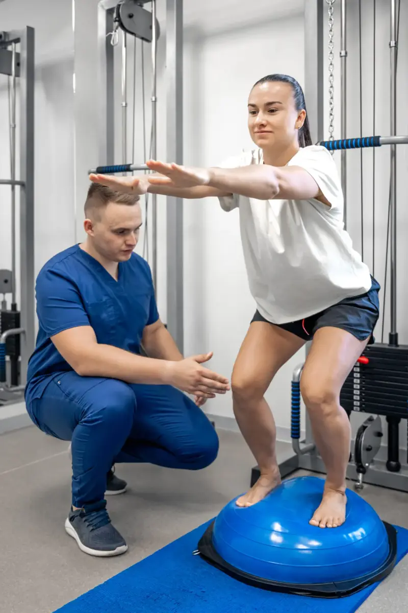 Clinician coaching an athlete through a squat on a balance trainer during ACL rehab