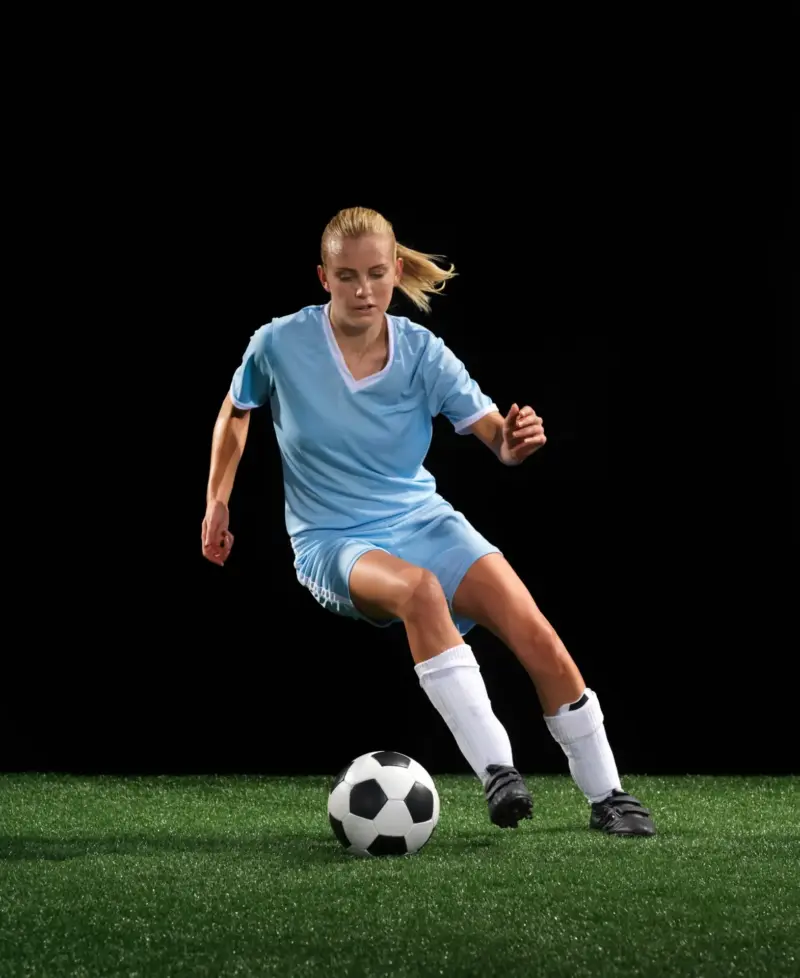 Female soccer player dribbling a ball against a dark background