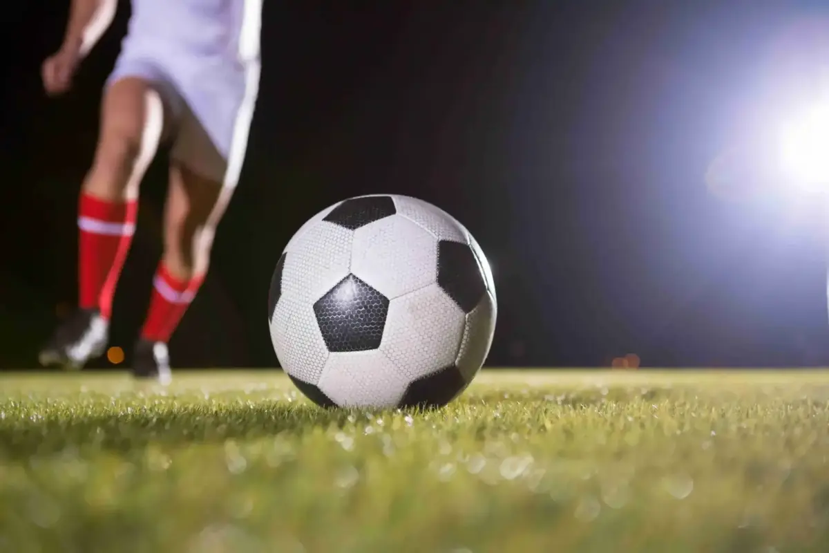 Soccer ball on grass under stadium floodlights as a player approaches