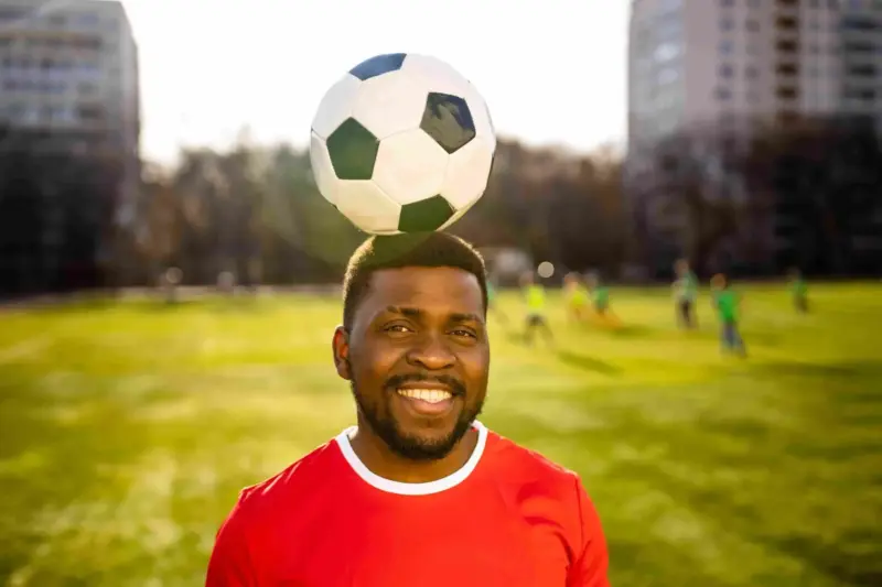 Smiling soccer player balancing a ball on his head in a stadium